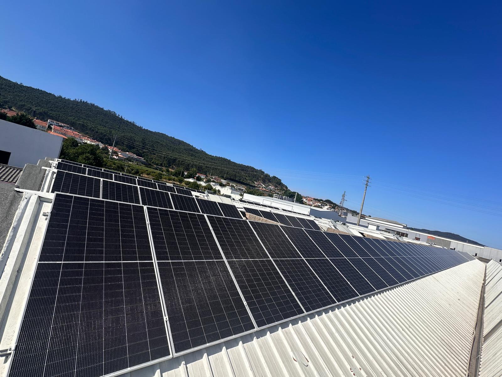 Painéis solares num telhado industrial com montanha ao fundo sob céu azul